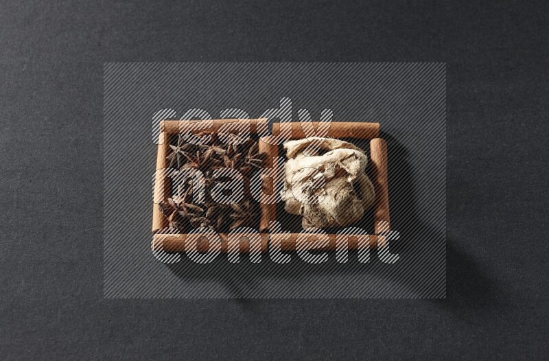 مربعان من أعواد القرفة ممتلئان باليانسون النجمي والزنجبيل المجفف علي خلفية سوداء