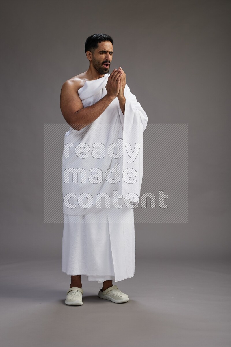 A man wearing Ehram standing showing how to sneeze on gray background