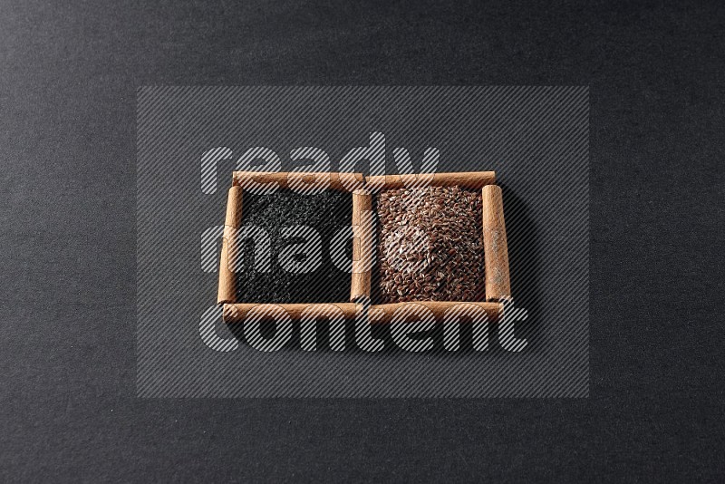 2 squares of cinnamon sticks full of flaxseeds and black seeds on black flooring