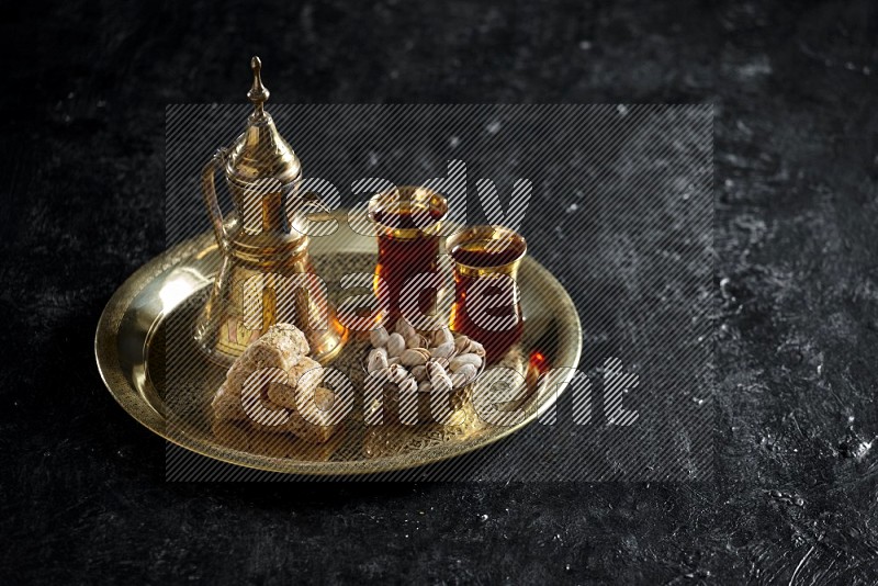 Oriental sweets with nuts and a drink on a metal tray in a dark setup