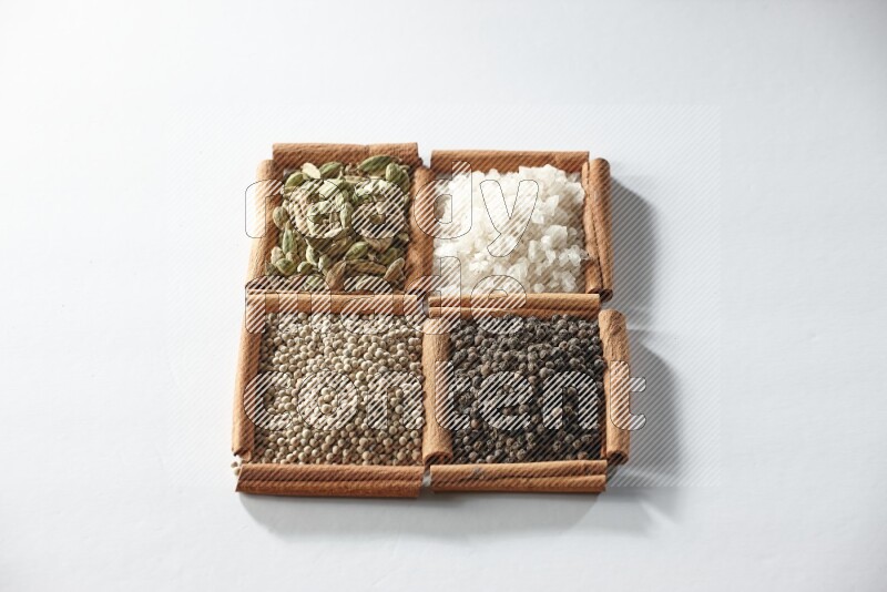 4 مربعات من أعواد القرفة ممتلئة بالهيل والملح والفلفل الأبيض والفلفل الأسود على أرضية بيضاء