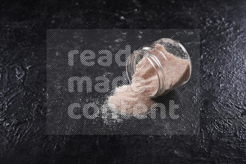 A glass jar full of fine himalayan salt on black background