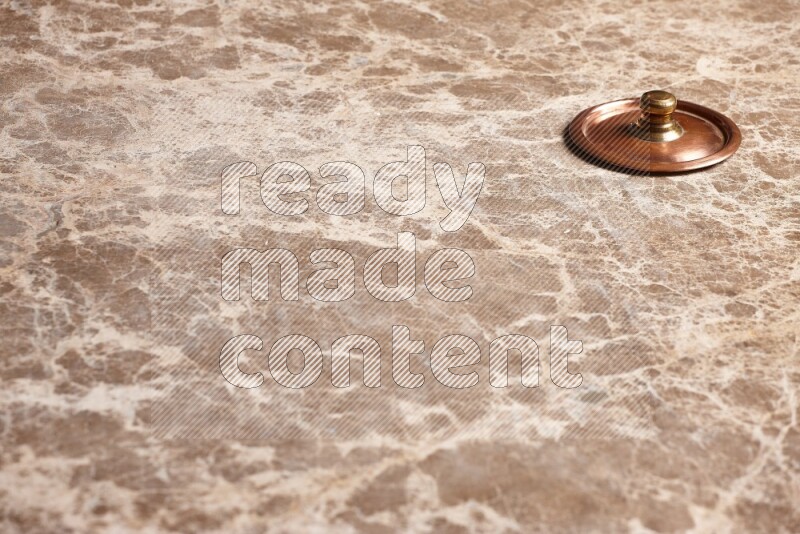 A small copper pot lid on beige marble background