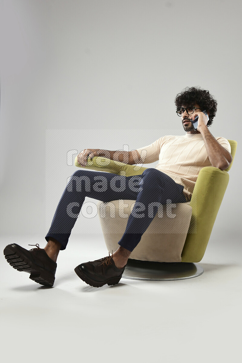 رجل يرتدي ملابس كاجوال يجلس علي كرسي و يتحدث في الهاتف علي خلفية بيضاء