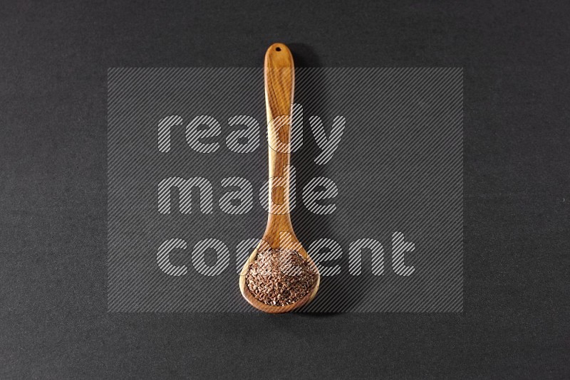 A wooden ladle full of flaxseeds on a black flooring