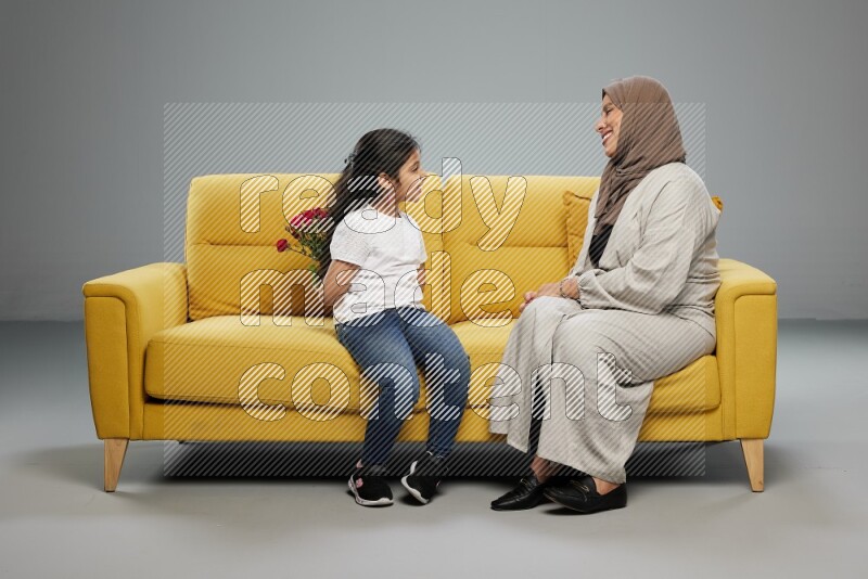 A girl sitting hiding flowers behind her back for her mother on gray background