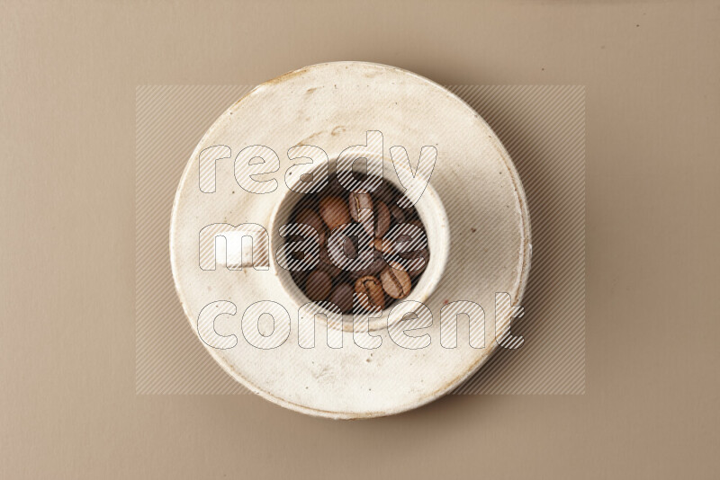 A beige pottery cup full of roasted coffee beans on beige background