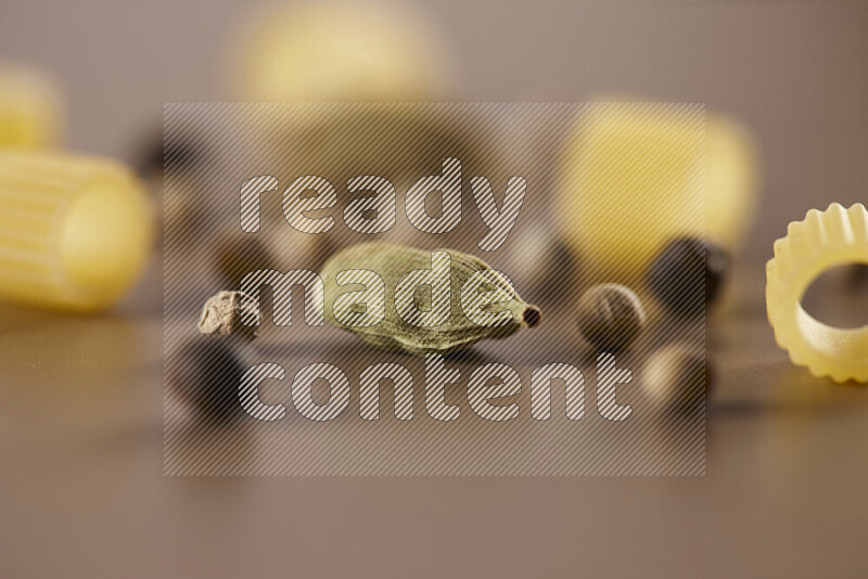 Raw pasta with different ingredients such as cherry tomatoes, garlic, onions, red chilis, black pepper, white pepper, bay laurel leaves, rosemary and cardamom on beige background