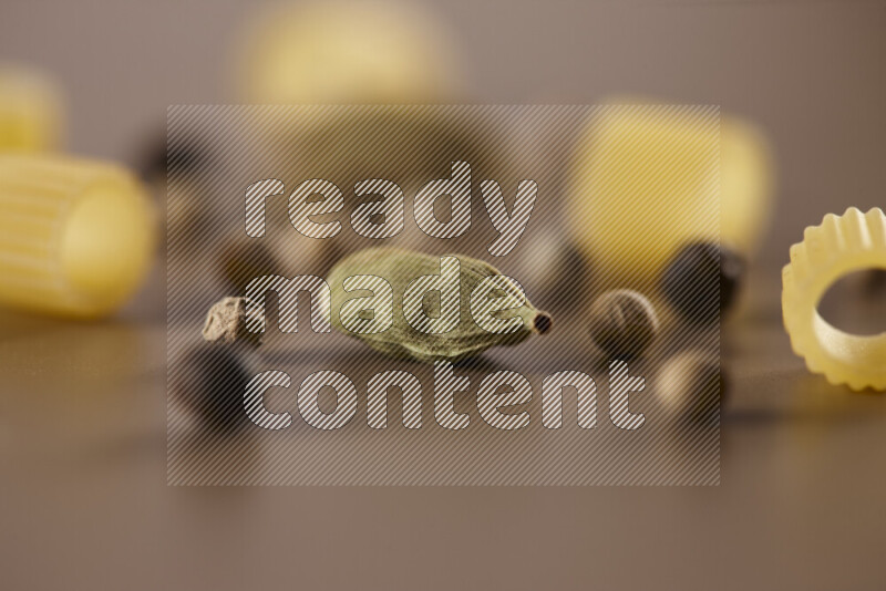 Raw pasta with different ingredients such as cherry tomatoes, garlic, onions, red chilis, black pepper, white pepper, bay laurel leaves, rosemary and cardamom on beige background