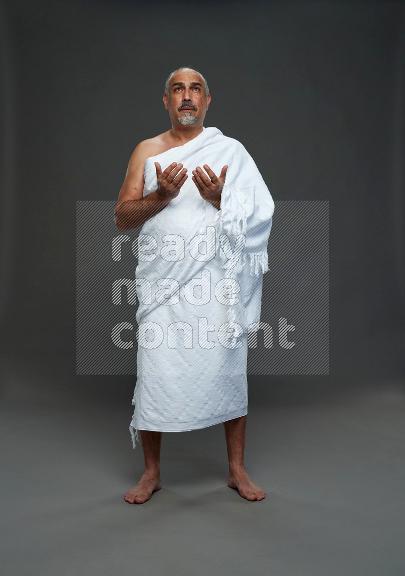 A man wearing Ehram Standing dua'a on gray background