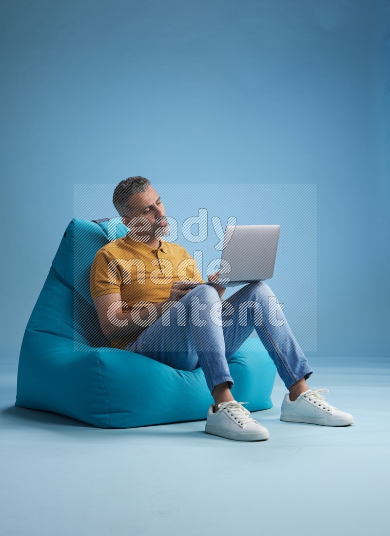 A man sitting on a blue beanbag and working on laptop