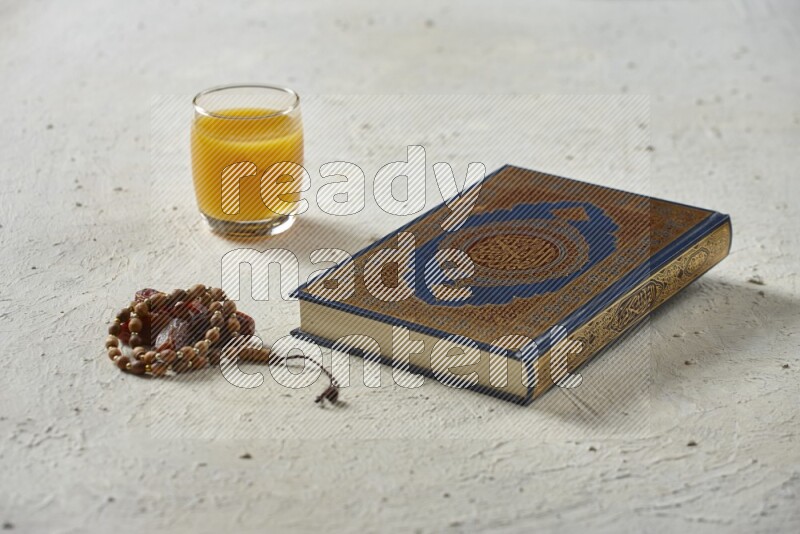 Quran with dates, prayer beads and different drinks all placed on textured white background