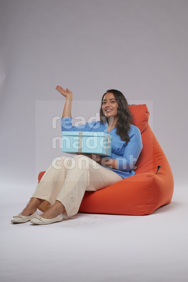 A woman sitting on an orange beanbag and opining a gift