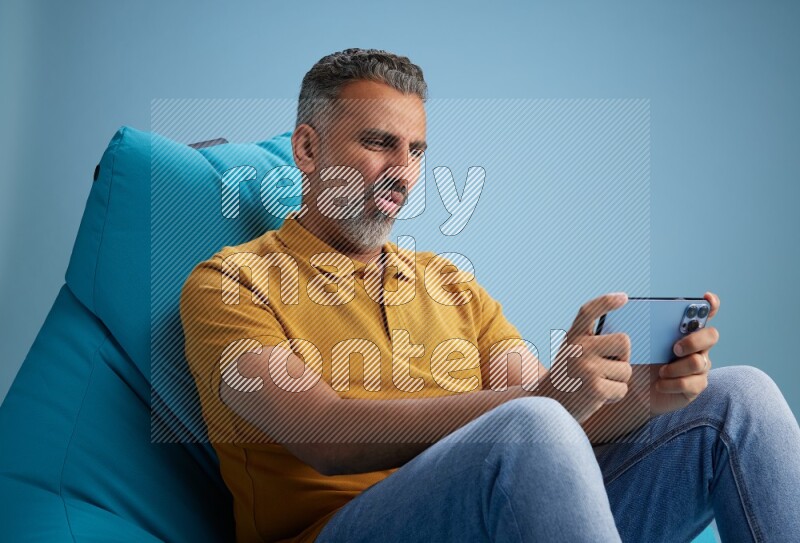 A man sitting on a blue beanbag and playing on phone