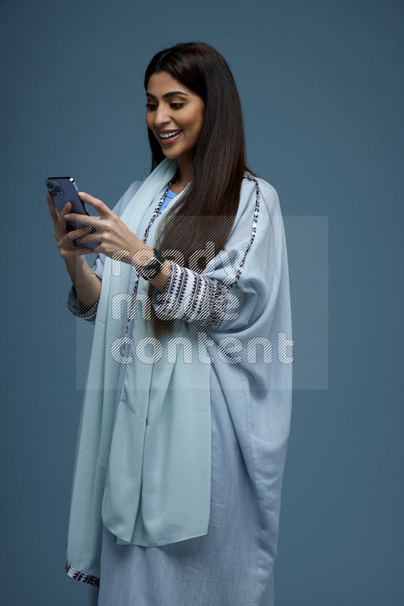 A Saudi woman Texting in a blue background wearing blue Abaya with no hijab