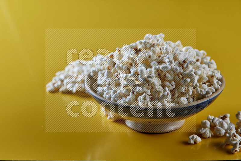 A multicolored ceramic plate full of popcorn with popcorn beside it on a yellow background in different angles