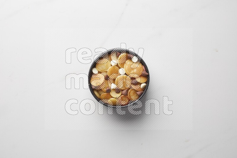 Top-view shot of mixed chocolate chips cereal pancakes in a round bowl on white background