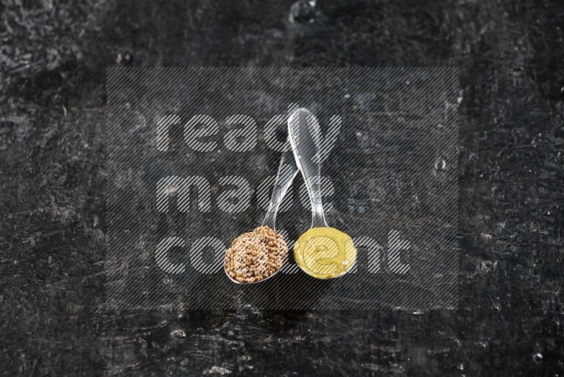 Two metal spoons, one filled with mustard seeds and the other with mustard paste on black background