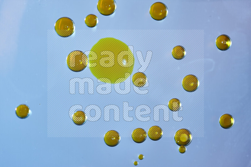 Close-ups of abstract yellow watercolor drops on oil Surface on blue background