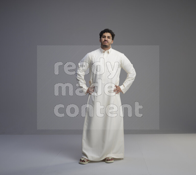 A Saudi man standing wearing thob interacting with the camera on gray background