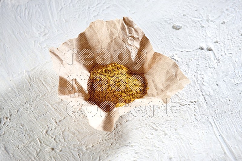 Turmeric powder in a crumpled piece of paper on textured white flooring