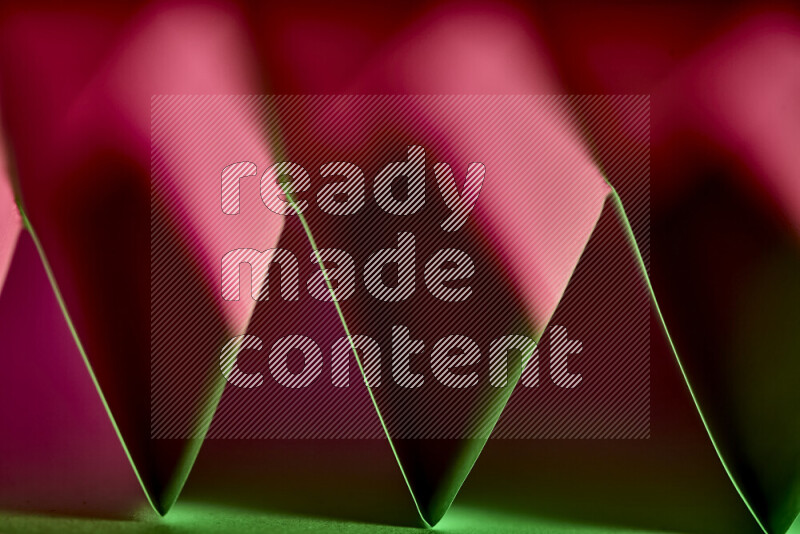 A close-up abstract image showing sharp geometric paper folds in green and red gradients