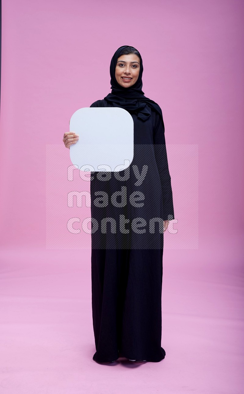 Saudi woman wearing pink ribbon on Abaya standing holding social media signs on pink background