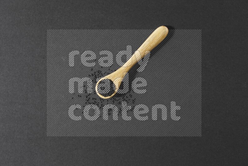 ملعقة خشبية ممتلئة بحبة البركة مع بعض الحبوب منتشرة بجانبها على أرضية سوداء