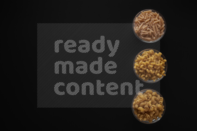 Different pasta types in 3 glass bowls on black background
