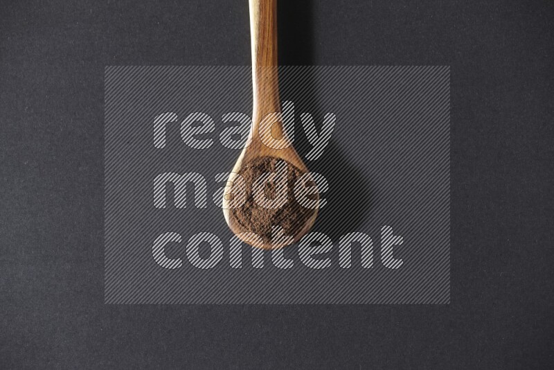 A wooden ladle full of cloves powder on a black flooring