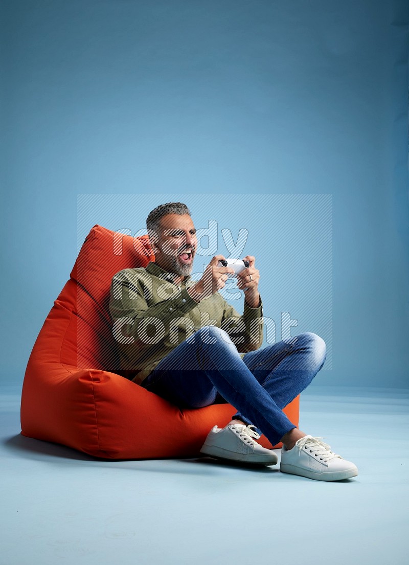 A man sitting on an orange beanbag and gaming with joystick