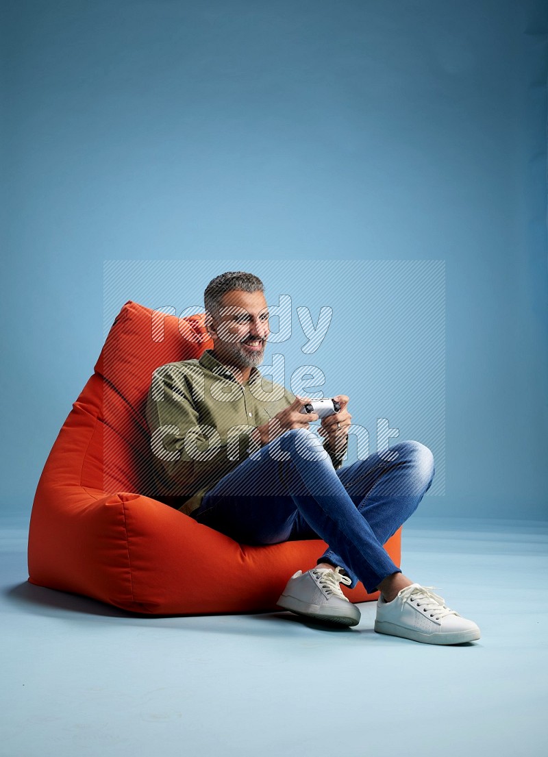 A man sitting on an orange beanbag and gaming with joystick