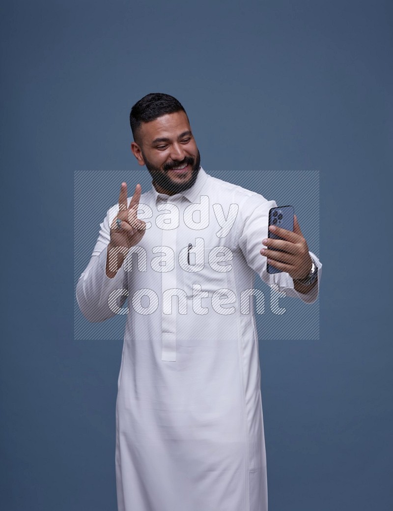 رجل سعودي يرتدي ثوب ابيض ويتصور بجواله