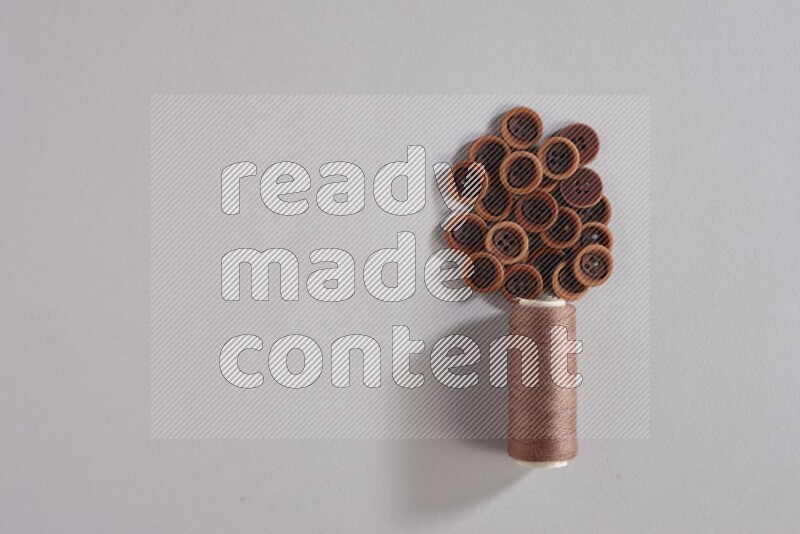 A brown sewing thread spool with colored buttons on grey background