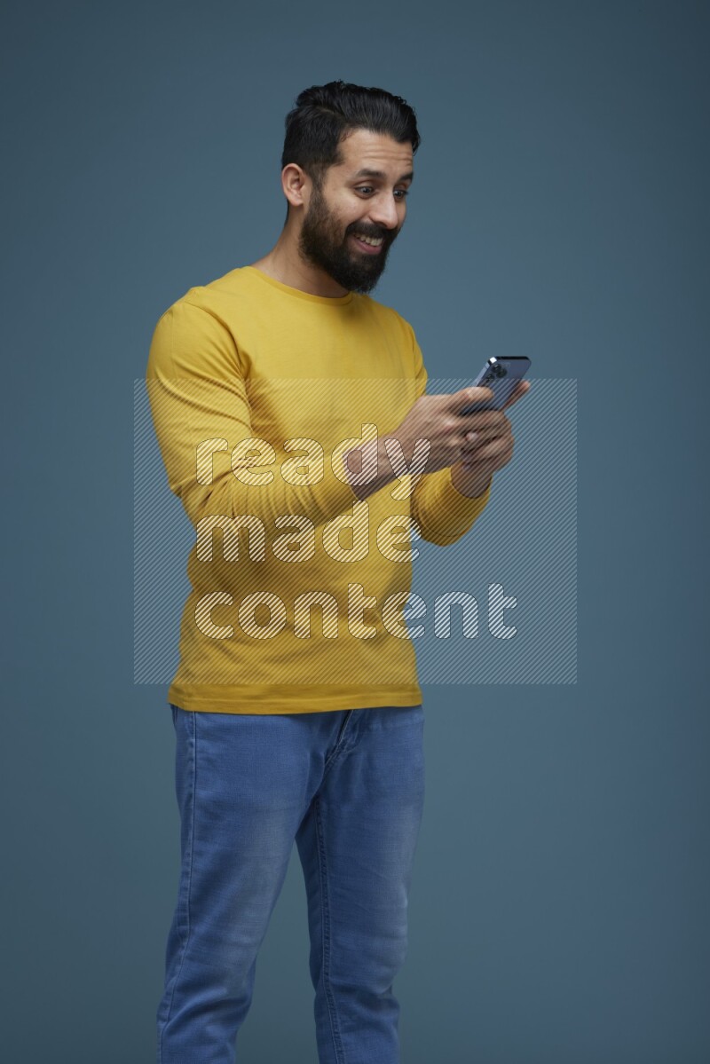 Man typing on his phone in a blue background wearing a yellow shirt