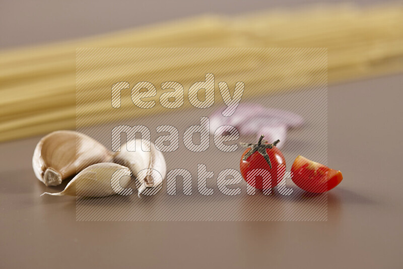 Raw pasta with different ingredients such as cherry tomatoes, garlic, onions, red chilis, black pepper, white pepper, bay laurel leaves, rosemary and cardamom on beige background