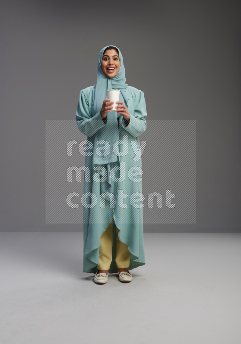 Saudi Woman wearing Abaya standing  holding paper cup on Gray background