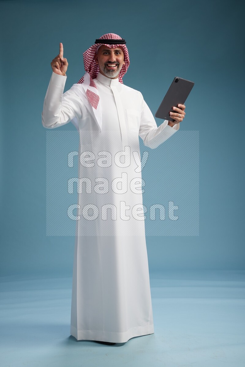 Saudi man wearing thob and shomagh with tablet on Blue background