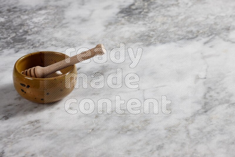 Multicolored pottery bowl with wooden honey dipper in it on grey marble background