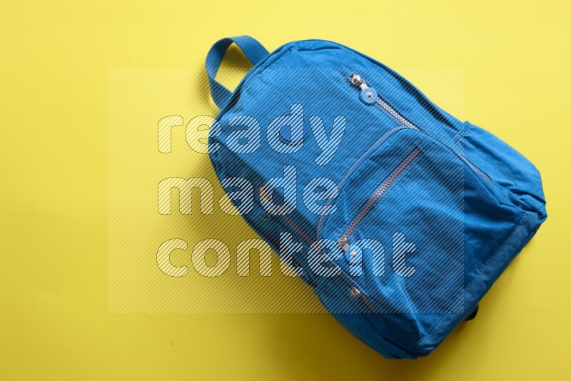 A blue school bag placed on yellow background