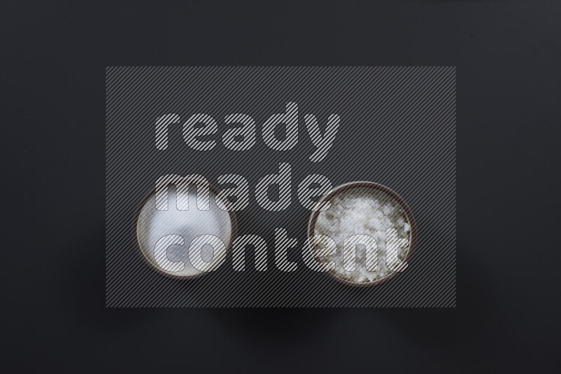 وعاء فخاري ممتلئ بملح الطعام الناعم وملح البحر الخشن على خلفية سوداء