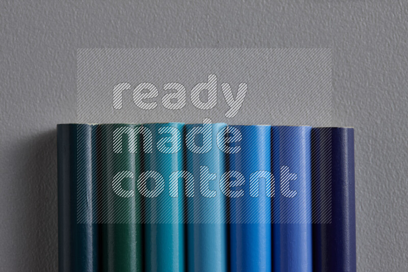 A collection of colored pencils arranged showcasing a gradient of blue hues on grey background