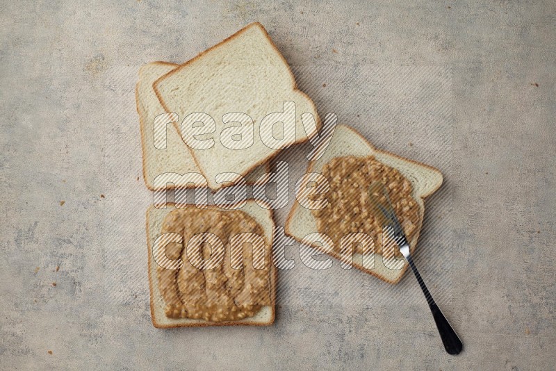 crunchy peanut butter on white toast and white toast slices on a light blue textured background