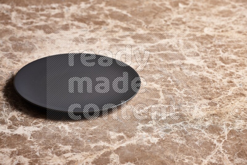A black ceramic circular plate on beige marble background