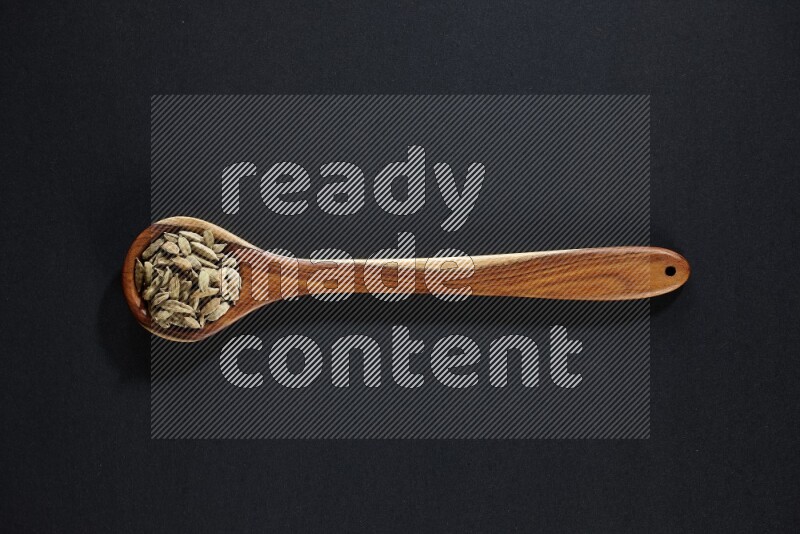 A wooden ladle full of cardamom on black flooring