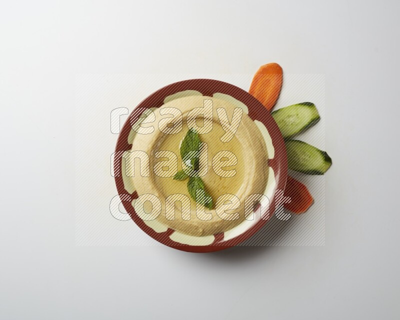 Hummus in a traditional plate garnished with mint on a white background