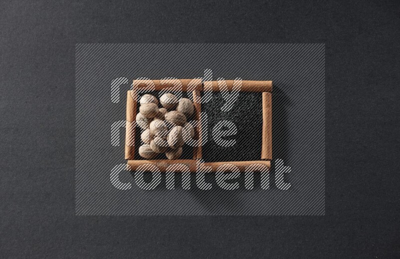 مربعان من أعواد القرفة ممتلئان بحبة البركة السوداء وجوزة الطيب علي خلفية سوداء