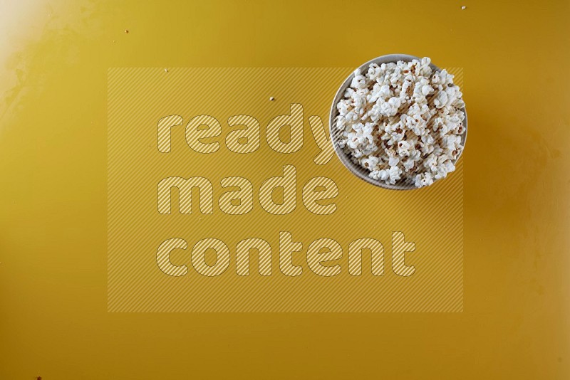 A white pottery bowl full of popcorn on a yellow background in different angles