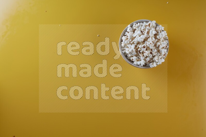 A white pottery bowl full of popcorn on a yellow background in different angles