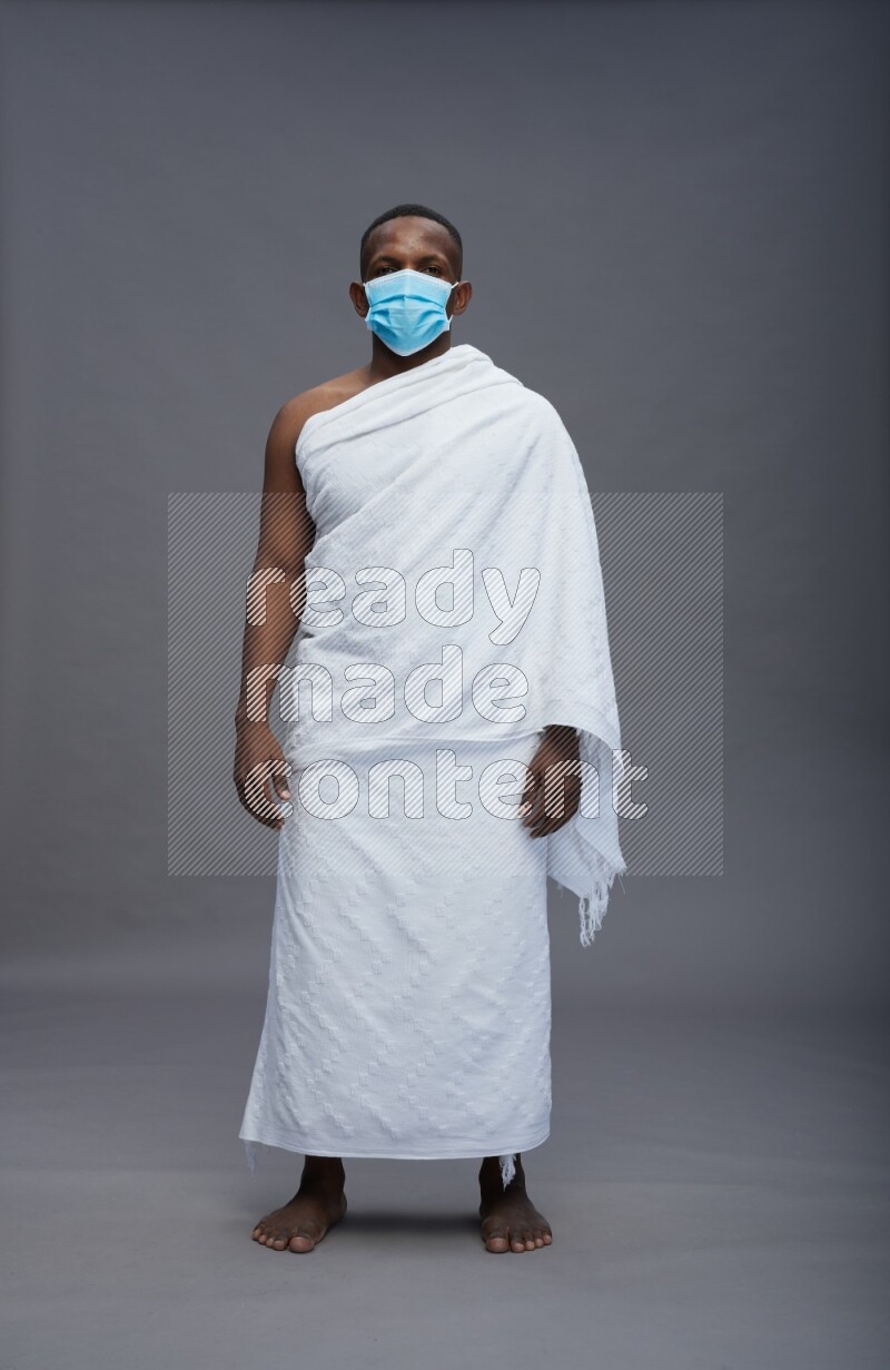 A man wearing Ehram with face mask Standing Interacting with the camera on gray background